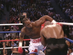 A boxer in white shorts throws a punch at an opponent in black shorts during a match.