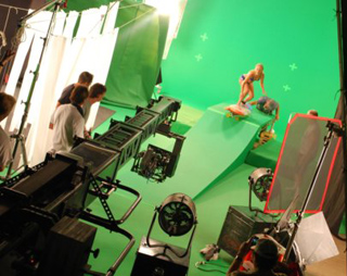 Film crew and equipment on a green screen studio set with a ramp and lighting.