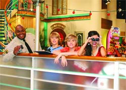 A man and three children lean against a counter in a brightly lit, decorated indoor space.