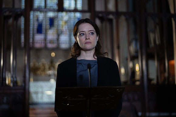 A woman with dark hair looking upward while standing behind a lectern in a dimly lit church.