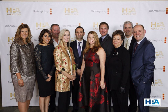 A group of ten men and women in formal attire posing in front of an HPA Awards 2016 backdrop.
