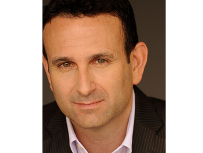 Close-up portrait of a man with dark hair and light eyes wearing a dark pinstripe suit and light collared shirt.