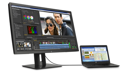 Large computer monitor showing video editing software next to a small laptop connected by a cable.