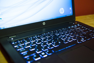 Close-up of an HP laptop with a glowing blue backlit keyboard and a bright screen.