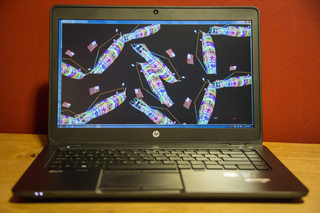 A black laptop on a wooden surface displaying a dark screen with colorful, abstract geometric patterns.
