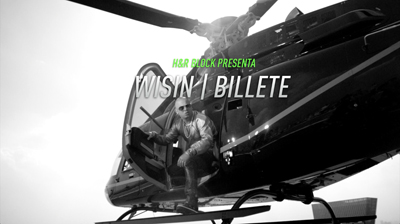 A man in sunglasses sits in the open doorway of a black helicopter against a bright sky.