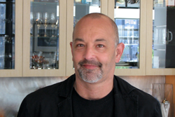 A bald man with a grey goatee wearing a black shirt and jacket.