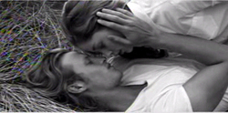 Black and white close-up of two people lying in grass with their foreheads touching.