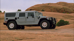 A silver four-door Hummer parked on a dirt path with red rock hills in the background.