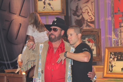 A man in a black cowboy hat and red shirt stands beside a man in a black t-shirt.