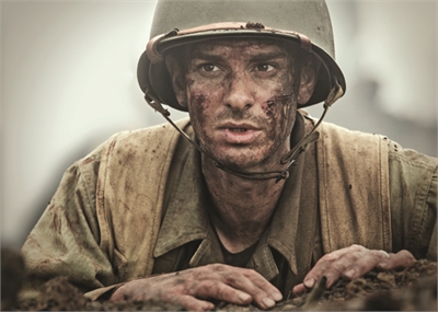 A soldier with a dirt-streaked face wearing a helmet and tan uniform, looking upward from a trench.