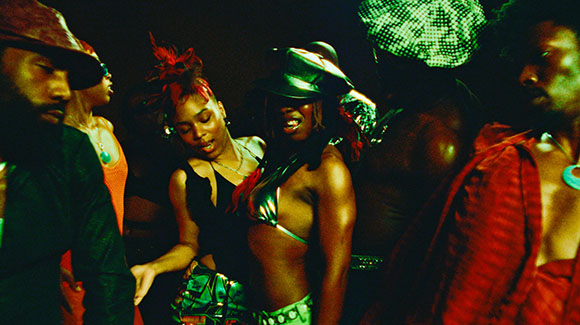 A group of people dancing closely together in a dark room with vibrant green and red lighting.