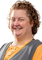 A woman with curly brown hair and a gray vest over an orange shirt smiles.