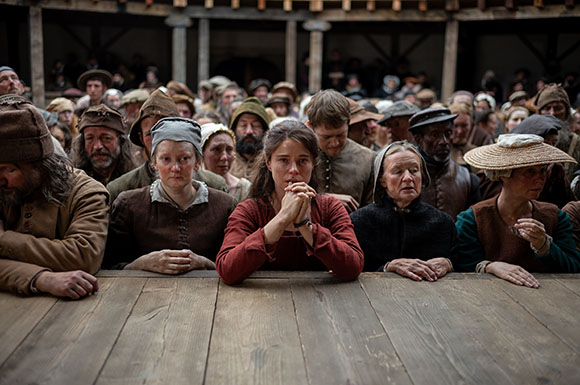 A large group of people in historical attire gathered closely together in a wooden building.