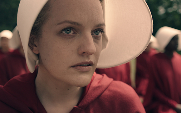 Close-up of a woman with light eyes wearing a white bonnet and red hooded garment.