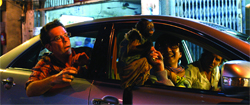 A man in glasses looks startled as a small monkey sits in the passenger seat of a car at night.