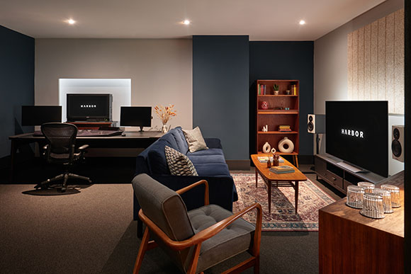 A modern living room with a blue sofa, wooden armchair, and coffee table next to a home office setup.