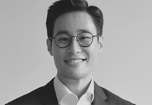 Black and white headshot of a smiling man wearing round glasses and a suit jacket.