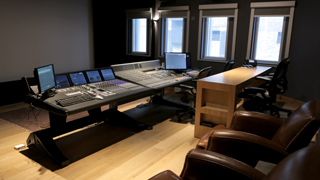 A large audio mixing console with multiple computer monitors in a dark recording studio.