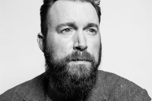 Black and white close-up portrait of a man with a full beard looking slightly to the side.