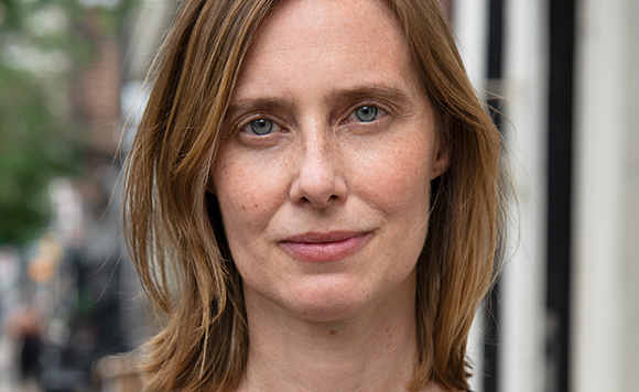 Close-up portrait of a woman with light brown hair and blue eyes looking directly at the camera.