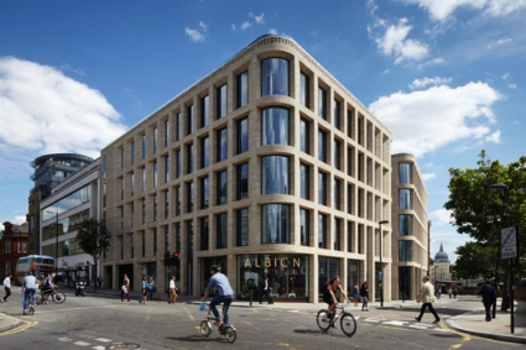 A multi-story light stone building with large windows on a city street corner under a blue sky.