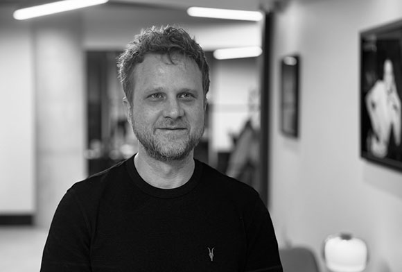 Black and white portrait of a man with short hair and a beard wearing a dark crewneck shirt.