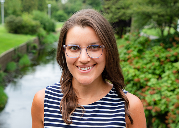 A smiling woman with long brown hair and glasses wearing a striped sleeveless top.