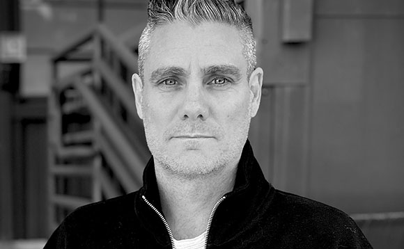 Black and white close-up portrait of a man with short hair looking directly at the camera.
