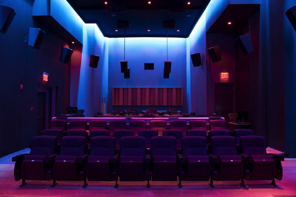 A dark movie theater with rows of purple seats and blue accent lighting on the walls.