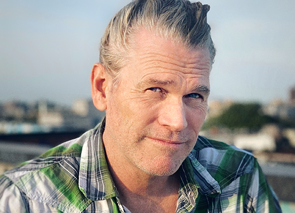 Close-up portrait of a man with gray hair and blue eyes wearing a green and white plaid shirt.