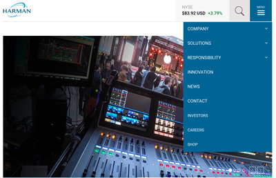 An audio mixing console in the foreground overlooks a crowd at an indoor event with stage lighting.