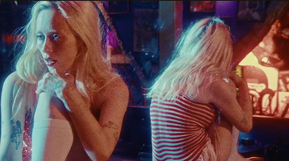 Two blonde women in a dark, moody setting with blue and red lighting.