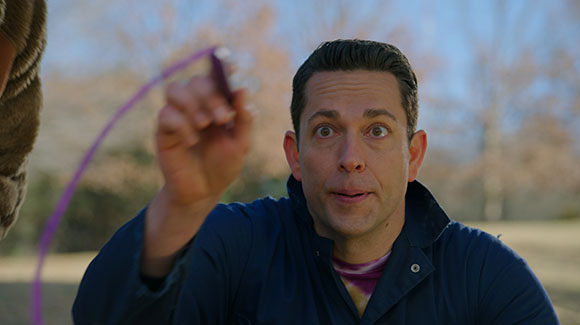 A man in a blue jacket looks up with wide eyes while holding a purple jump rope.