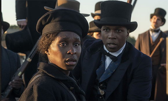A Black woman and man in period clothing look off-camera with worried expressions.