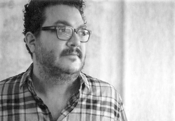 Black and white close-up of a man with curly hair, glasses, and a beard wearing a plaid shirt.