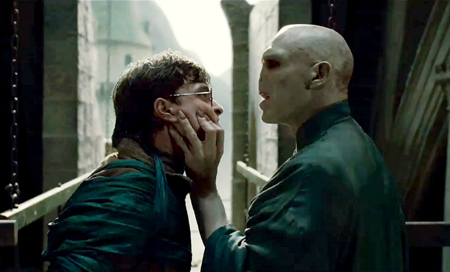 A bald man holds the face of a man with glasses in a tense close-up.