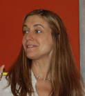 A woman with long brown hair smiling and looking toward the left against a red background.