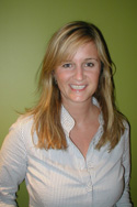 A smiling woman with blonde hair wearing a white patterned button-down shirt against a green background.
