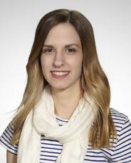 A woman with long blonde hair smiling, wearing a blue and white striped shirt and a white scarf.