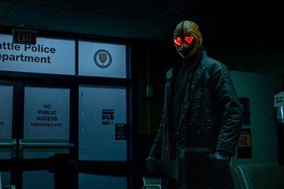 A person wearing a gold mask with glowing red heart eyes stands before a Seattle Police Department sign.
