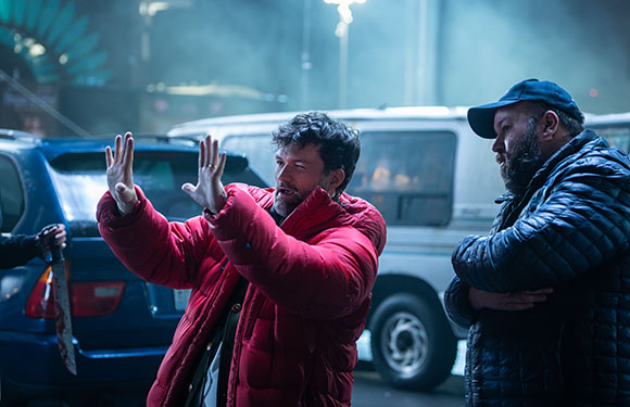 A man in a red puffer jacket raises his hands defensively while a man in a blue jacket watches him.