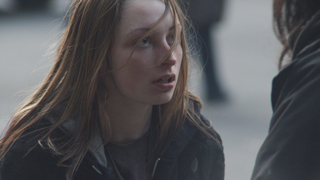 A young woman with long blonde hair looks upward with a worried expression while talking to someone.