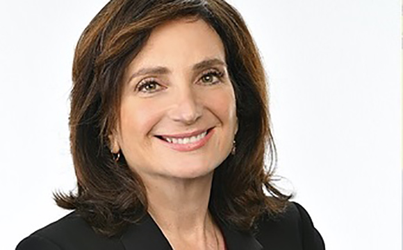 A smiling woman with shoulder-length brown hair wearing a black blazer against a white background.