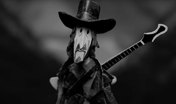 Black and white papercraft figure of a character in a wide-brimmed hat holding a guitar.