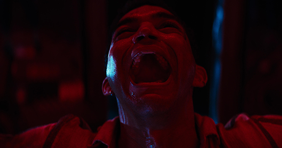 A man with his mouth wide open in a scream, illuminated by red and blue light.