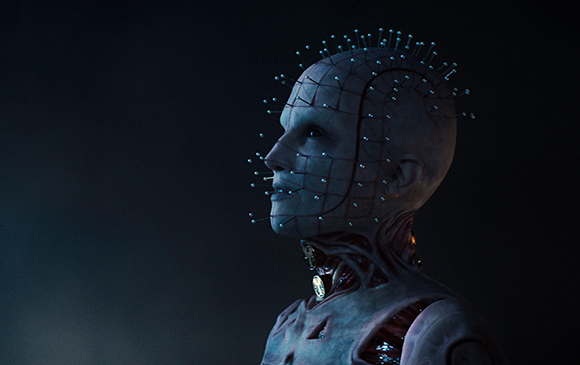 Profile of a pale humanoid figure with a grid pattern on its face and pins protruding from its head.