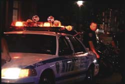 A white police car with flashing emergency lights parked on a street at night.