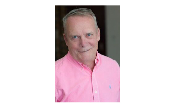 A middle-aged man with short grey hair and blue eyes wearing a pink button-down shirt.