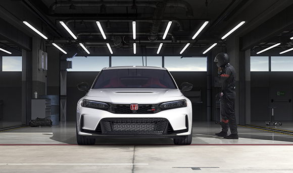 A white Honda Civic Type R parked in a dimly lit garage next to a person in dark clothing.